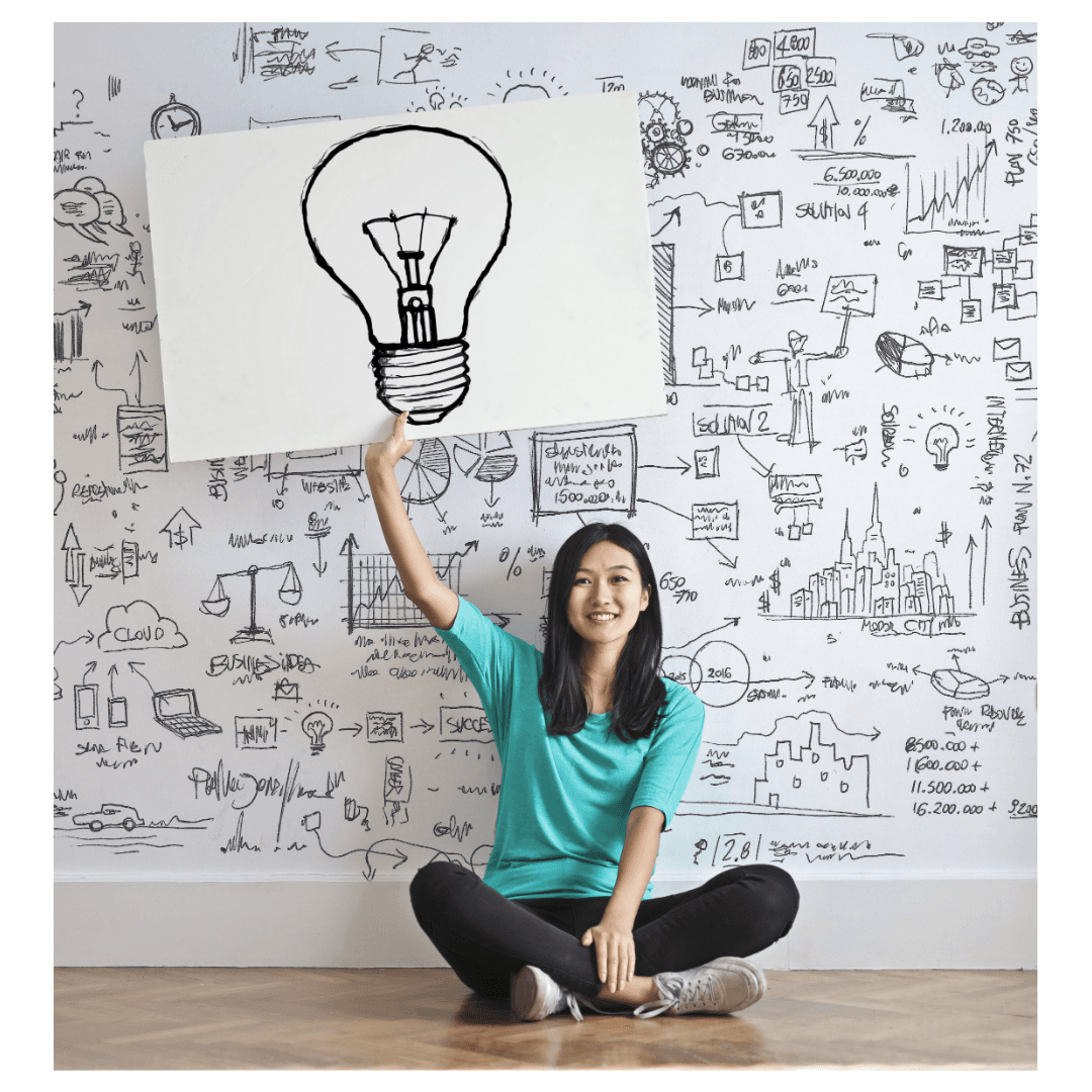 A smiling woman sitting cross-legged, holding a light bulb sign in a creative workspace, symbolizing the importance of creativity and innovative ideas in enhancing campaign effectiveness.