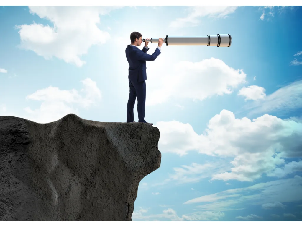 Businessman standing on the edge of a cliff looking through a large telescope, symbolizing the search for future opportunities and trends to stay competitive.