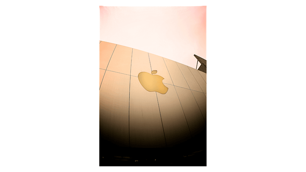 A close-up image of the Apple logo displayed prominently on a smooth surface, with soft lighting enhancing its golden hue against a minimalist background. The image conveys a sense of modern design and brand identity associated with Apple products.