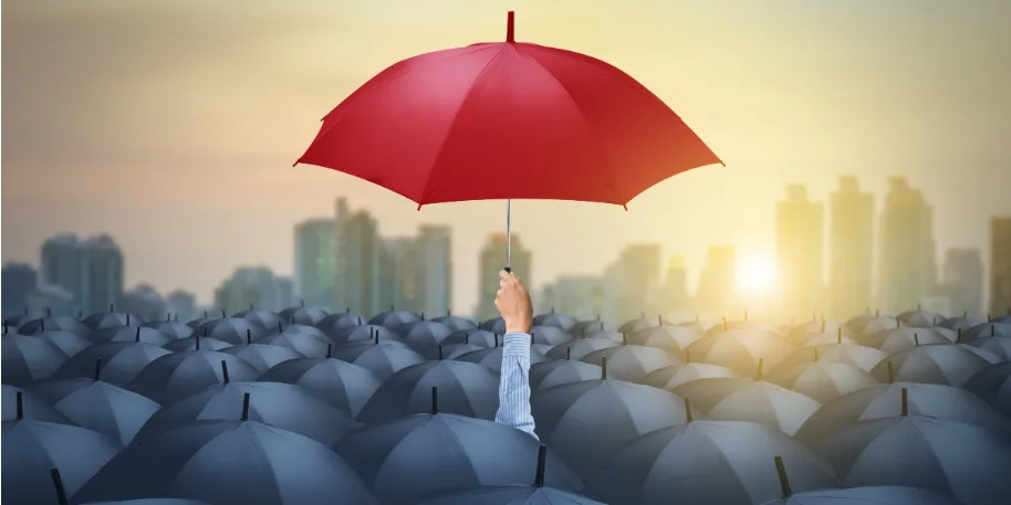 A single red umbrella held high above a sea of dark blue umbrellas, symbolizing standing out from the crowd or uniqueness in a competitive landscape, with a city skyline and a warm sunrise in the background.